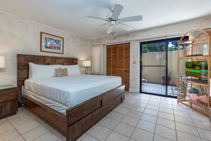 Ein Schlafzimmer mit einem großen Bett, einem Deckenventilator, einer Schiebetür zu einem Balkon und einer kleinen Zimmerpflanzenausstellung.