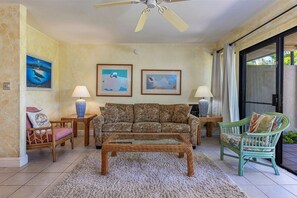 Ein Wohnzimmer mit einer Couch, zwei Beistelltischen, einem Couchtisch, einem Deckenventilator und einer Schiebetür aus Glas.