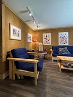 Una habitación acogedora con suelo de madera, un sofá azul, una silla de madera y una lámpara.
