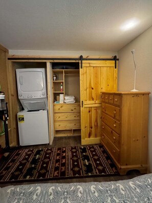Ein kleines Zimmer mit Waschmaschine, einem Holzschrank und einer eingebauten Regaleinheit.