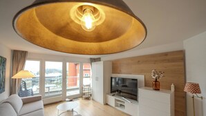 Una sala de estar moderna con un sofá, un televisor, suelo de madera y un ventanal grande.