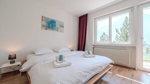 A bedroom with a bed, a nightstand, a lamp, a window with a view, and a painting on the wall. - Viktoria A12 by Arosa Vacations Appartement/Fewo, Dusche, WC, 1 Schlafraum by Interhome (Arosa)