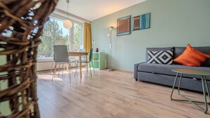 A room with a dining table, chairs, a sofa, a small table, and a floor lamp. - Viktoria A12 by Arosa Vacations Appartement/Fewo, Dusche, WC, 1 Schlafraum by Interhome (Arosa)