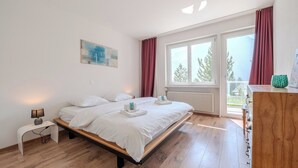 A bedroom with a bed, bedside table, lamp, artwork, window with curtains, and a view of trees. - Viktoria A12 by Arosa Vacations Appartement/Fewo, Dusche, WC, 1 Schlafraum by Interhome (Arosa)