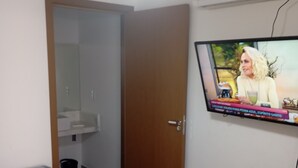 Une chambre à coucher avec un lit, un téléviseur fixé au mur, une porte et une petite fenêtre.