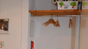 Et værelse med et knagered, en hængende frakke, et indrammet billede og et rødt brandalarmsymbol.