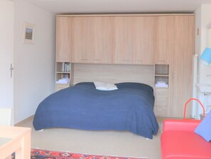 Ein Schlafzimmer mit Bett, Kleiderschrank, Nachttisch, einem roten Sessel und einer Lampe.