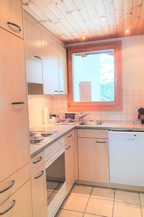 Eine Küche mit Holzausstattung, einem Einbauofen, einem Geschirrspüler und einem Fenster über der Spüle.