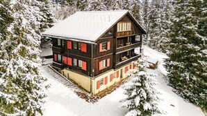 Useita kerroksia sisältävä puinen mökki, jossa on parvekkeet, ja sen ympärillä on lumipeitteisiä puita.