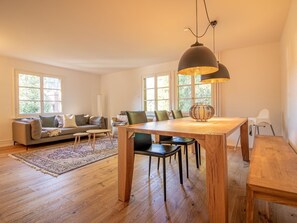 A spacious living room with a wooden dining table, a sofa, and a large window providing natural light. - Pradella EG by Arosa Holiday Appartement/Fewo, Dusche oder Bad, WC, 7-Bettwohnun by Interhome (Arosa)