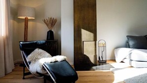 Ett modernt vardagsrum med en svart lädersoffa, en svart fåtölj med en vit pläd, en golvlampa och en dekorativ vas med torkade vassstrån.
