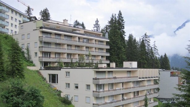 Un immeuble résidentiel à plusieurs étages, doté de balcons et entouré de verdure et d’arbres.