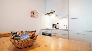 Une cuisine avec des meubles blancs, une table en bois et un panier contenant des brochures.