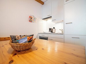 A kitchen with white cabinets, a wooden table, and a basket containing brochures. - Irmella 10 by Arosa Holiday Appartement/Fewo,  , 3-Bettwohnung Irmella 10 by Interhome (Arosa)