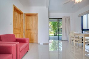 A spacious room with a red sofa, wooden doors, a dining table with chairs, and a view of greenery outside. - Horizon Homes By Suerte Tour (Potrero)