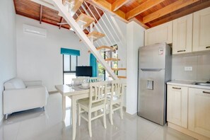 Una cocina moderna con refrigerador empotrado, escalera de madera y un comedor con mesa y sillas blancas.