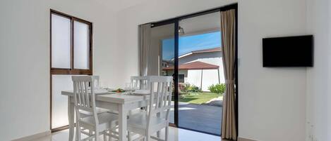 A modern dining area with a white table and chairs, a ceiling fan, a sliding glass door leading to a patio, and a mounted TV.