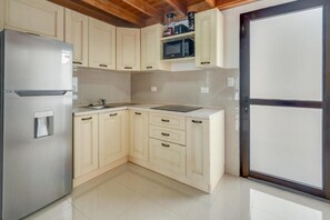 A kitchen with light-colored cabinets, a stainless steel refrigerator, a microwave, and a black countertop.
