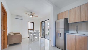A modern kitchen with wooden cabinets, a stainless steel refrigerator, and a dining area with white chairs.