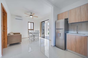 A modern kitchen with wooden cabinets, a stainless steel refrigerator, and a dining area with white chairs.