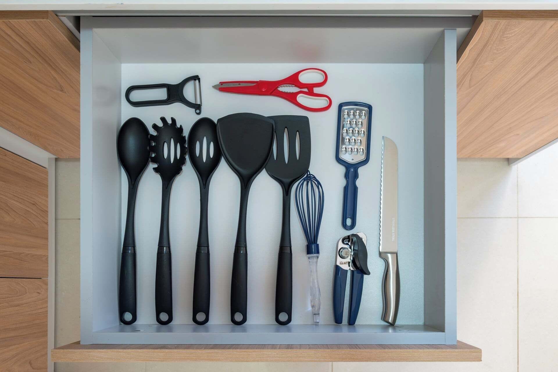 Un cajón con utensilios de cocina, incluyendo tijeras, un rallador, espátulas, un batidor y un cuchillo.