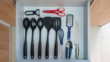 Un cajón con utensilios de cocina, incluyendo tijeras, un rallador, espátulas, un batidor y un cuchillo.