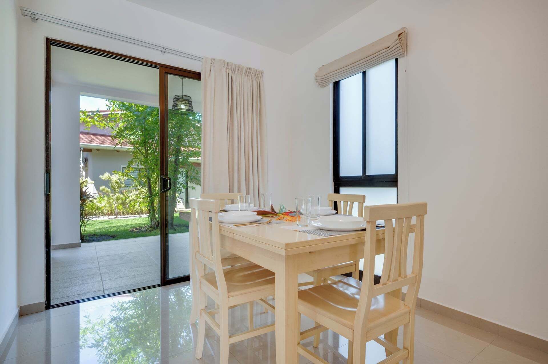 A dining area with a table set for two, a sliding glass door leading to a garden, and a window with a view of the outdoors.