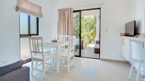 A modern room with a dining table, chairs, a sofa, a TV, and a sliding glass door leading to an outdoor area.
