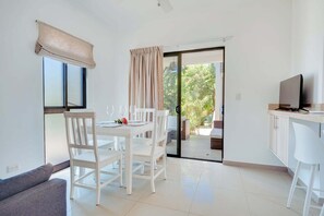A modern room with a dining table, chairs, a sofa, a TV, and a sliding glass door leading to an outdoor area.
