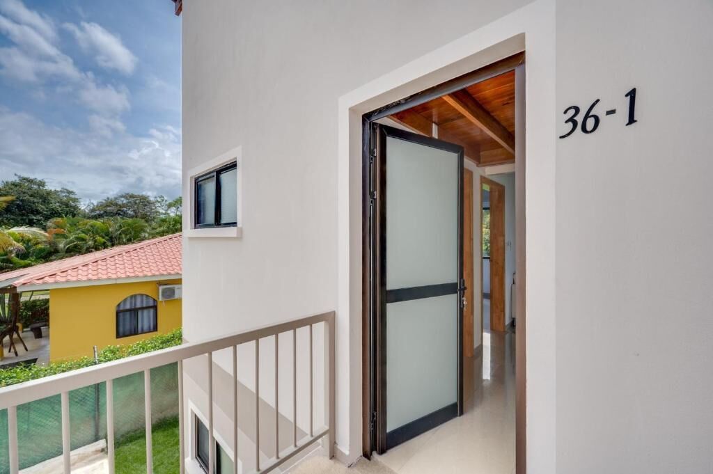 A balcony with a white railing, a glass door, and a view of a yellow building with a red roof.