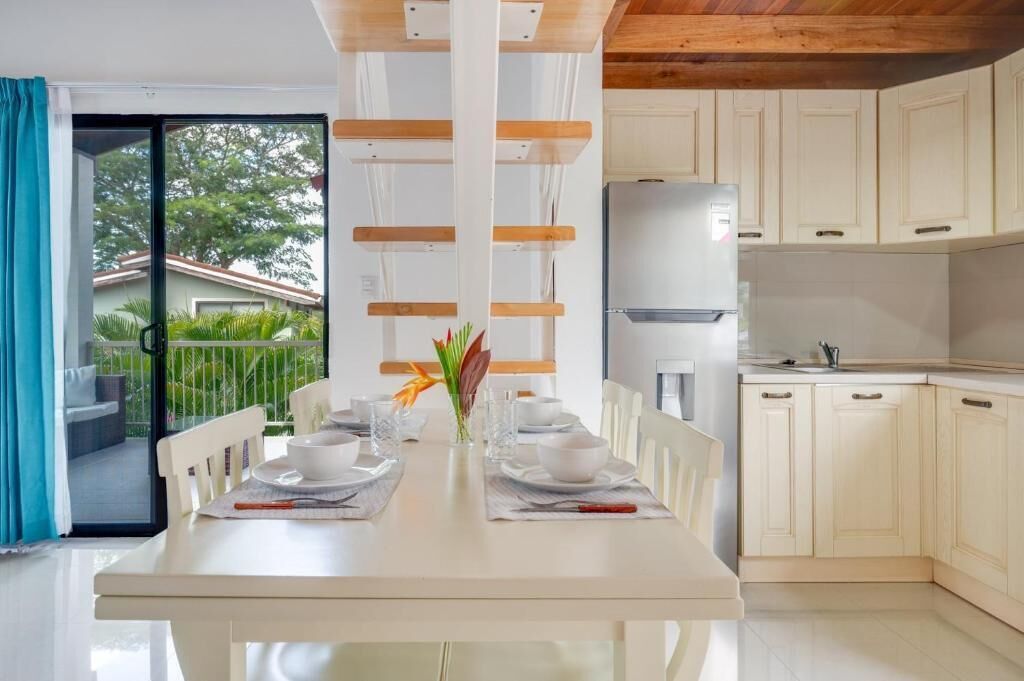 Cocina moderna con alacenas blancas, un refrigerador de acero inoxidable y un comedor con mesa dispuesta para dos.