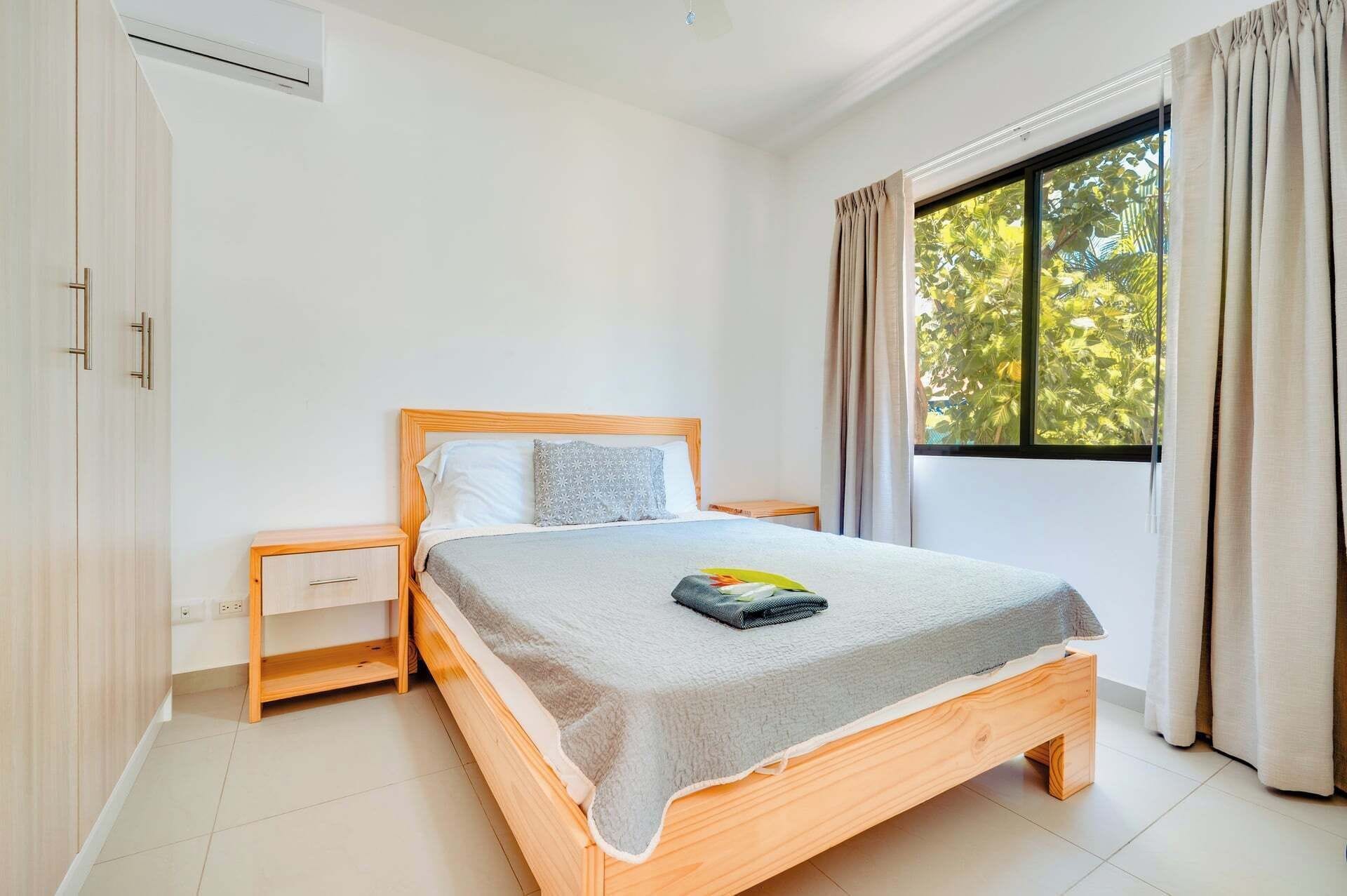 A bedroom with a wooden bed, a nightstand, a window with curtains, and a wardrobe.