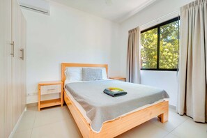 A bedroom with a wooden bed, a nightstand, a window with curtains, and a wardrobe.