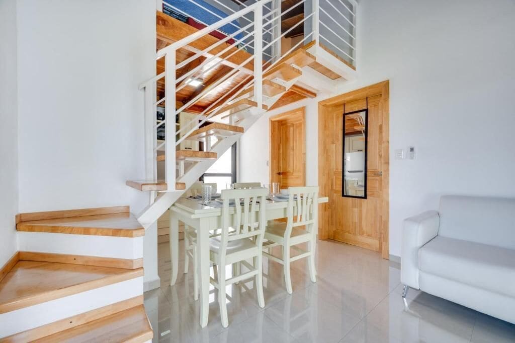 Un interior moderno con escalera, mesa de comedor, sillas y un sofá blanco.