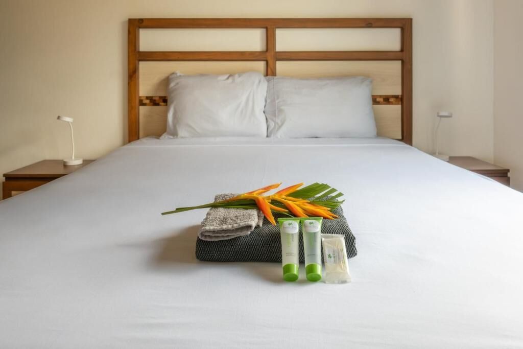 A neatly made bed with a wooden headboard, a folded towel, and toiletries on the bed.