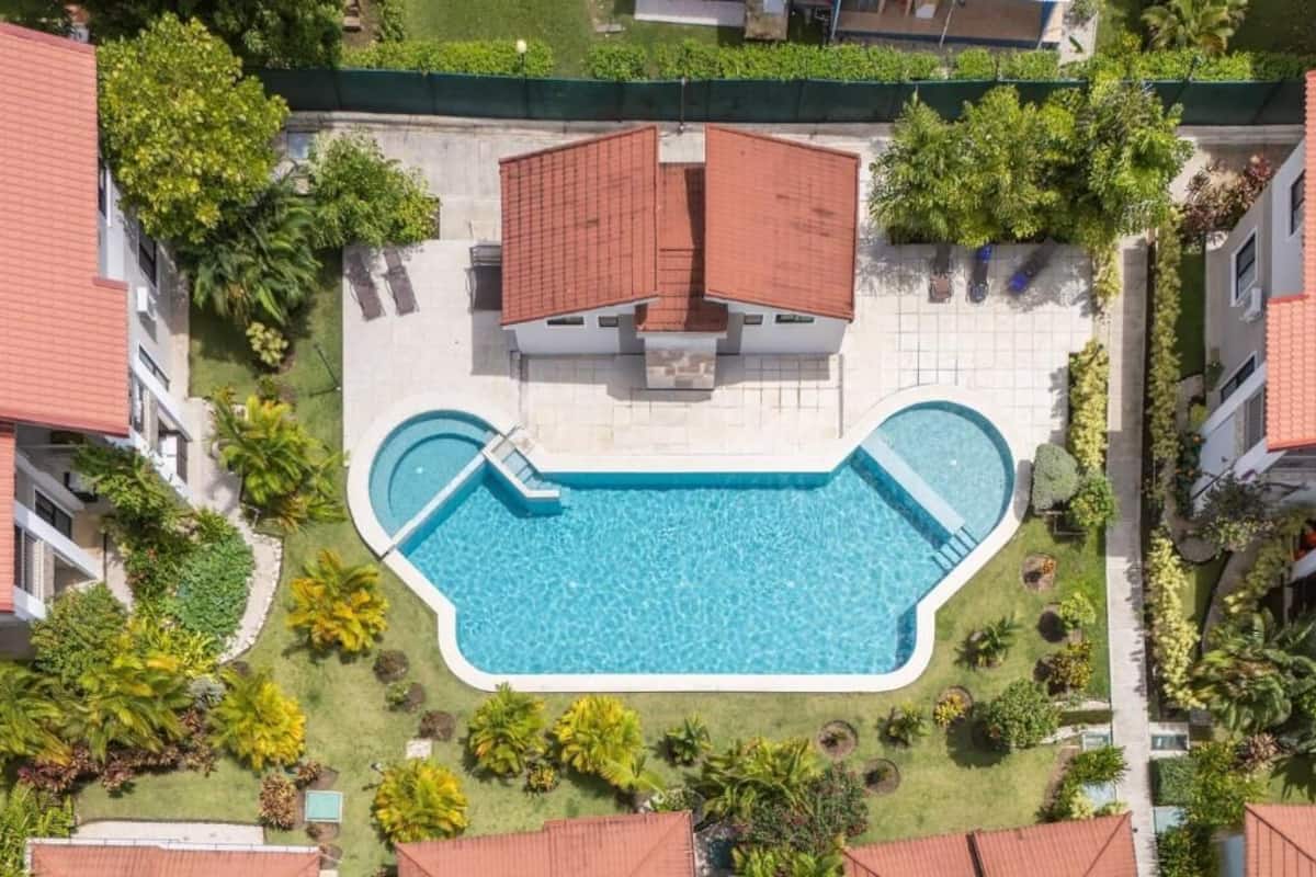 Vista aérea de una zona residencial con piscina, rodeada de vegetación y edificios colindantes.