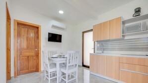 A modern kitchen with wooden cabinets, a built-in microwave, and a dining area with white chairs and a table set for two.