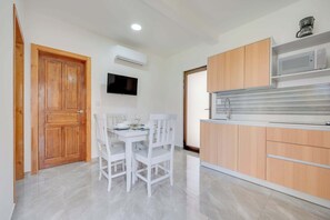 A modern kitchen with wooden cabinets, a built-in microwave, and a dining area with white chairs and a table set for two.