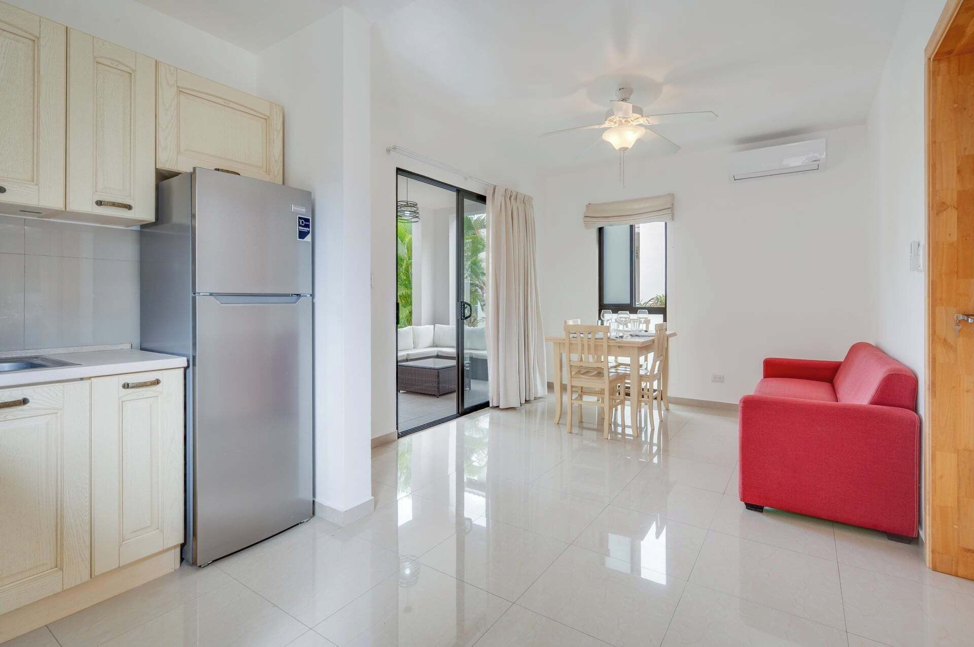 Una cucina moderna con frigorifero, un'area pranzo con tavolo e sedie, un divano rosso e una ventola a soffitto.