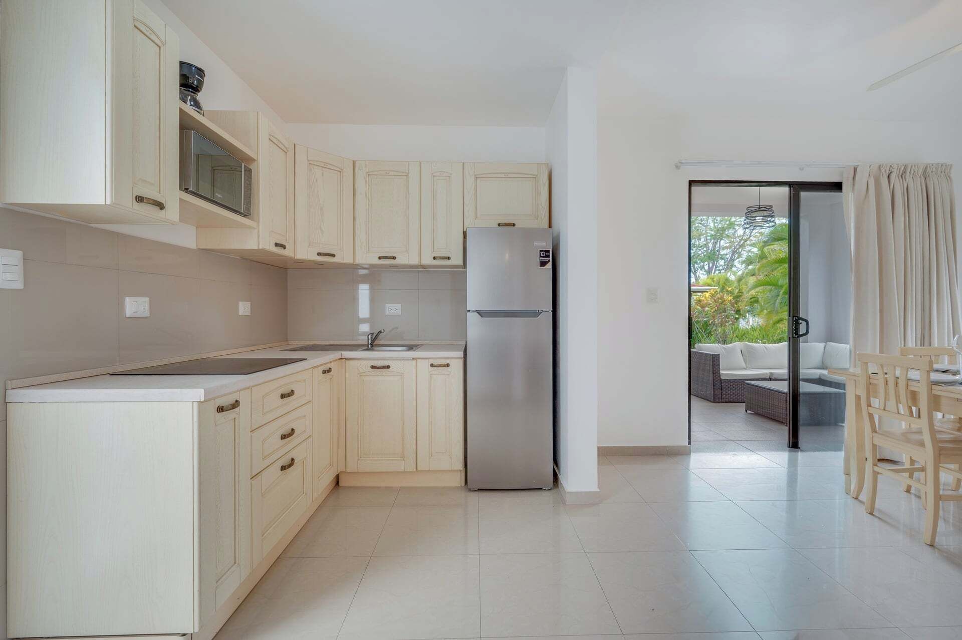 Una cocina moderna con armarios de tonos claros, un refrigerador de acero inoxidable y un comedor con mobiliario de mimbre.