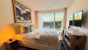 A bedroom with a large bed, a TV, a wooden dresser, and a view of the outdoors. - Eden 3 by Arosa Holiday Appartement/Fewo, Bad, WC, 6-Bettwohnung by Interhome (Arosa)