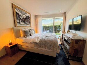 A bedroom with a large bed, a TV, a wooden dresser, and a view of the outdoors. - Eden 3 by Arosa Holiday Appartement/Fewo, Bad, WC, 6-Bettwohnung by Interhome (Arosa)