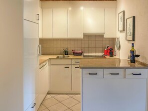 Een kleine keuken met witte kastjes, een spoelbak, een rood apparaat en een fles wijn op het aanrecht.