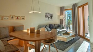 En moderne stue med et træspisebord, en sofa, et sofabord og et stort vindue med gardiner.