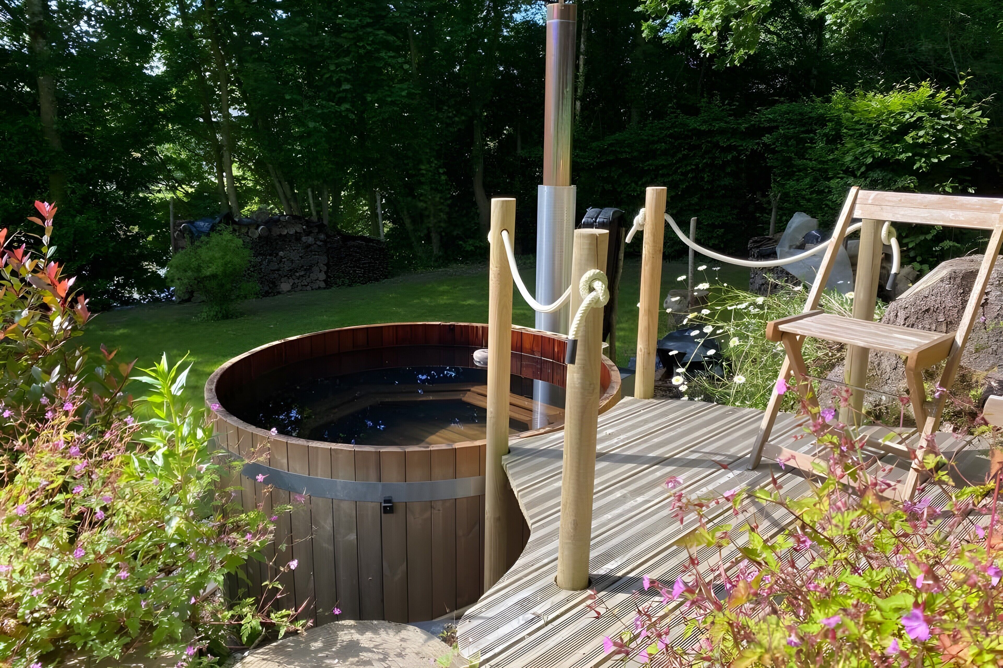 Een hottub op een houten terras, omringd door groen, met een touwbalkje.
