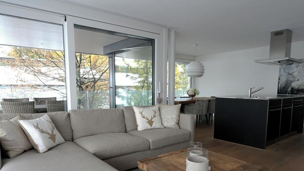 En moderne stue med en modulsofa, et træsofabord og et køkken med sort bordplade og stålemmer.