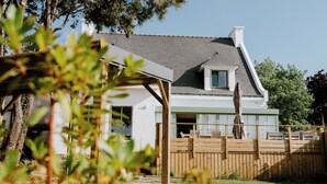 Una casa con techo inclinado, terraza de madera y patio trasero cercado.
