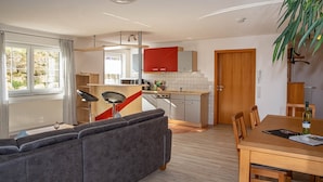 A modern kitchen with red cabinets, a dining area with a wooden table, and a grey sofa. - Apartment 'Haus 4, 2-Zimmer' with Lake View, Shared Terrace and Wi-Fi (Meersburg)