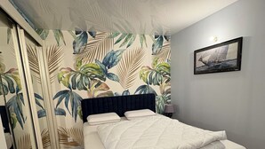 Ein Schlafzimmer mit Bett, Kleiderschrank, Spiegel und einer Wand mit tropischem Blattmuster.