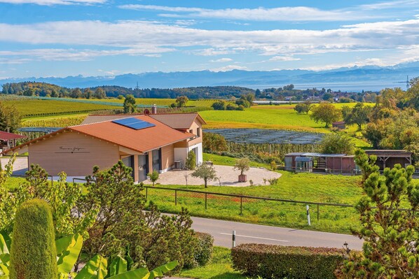 Uma casa com telhado vermelho, painéis solares e vista para montanhas e um lago.